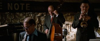 Movie still from “'Round Midnight” (1986), directed by Bertrand Tavernier – An older man in a suit and tie playing a contrabass; Medium shot, Over the shoulder angle