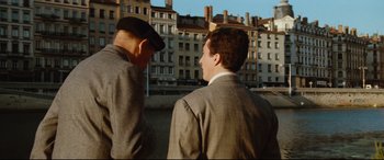 Movie still from “'Round Midnight” (1986), directed by Bertrand Tavernier – Two men in suits are standing in front of some buildings; Medium shot, Over the shoulder angle