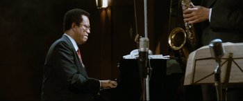 Movie still from “'Round Midnight” (1986), directed by Bertrand Tavernier – A man sitting at a piano in front of a microphone; Medium shot, Low angle