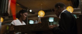 Movie still from “'Round Midnight” (1986), directed by Bertrand Tavernier – Two people sitting at a table in front of a bottle; Medium shot, Low angle