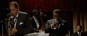 Movie still from “'Round Midnight” (1986), directed by Bertrand Tavernier – A man blowing into a trumpet in front of another man; Medium shot, Low angle