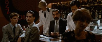 Movie still from “'Round Midnight” (1986), directed by Bertrand Tavernier – A group of men standing at a table in front of a bar; Medium shot, Over the shoulder angle