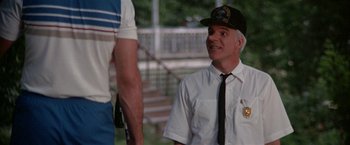 Movie still from “Roxanne” (1987), directed by Fred Schepisi – A man wearing a hat and a tie talking to another man; Medium shot, Over the shoulder angle