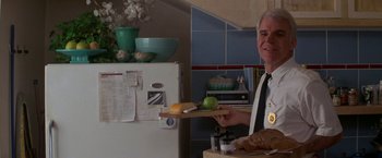 Movie still from “Roxanne” (1987), directed by Fred Schepisi – An older man holding a cutting board with a piece of fruit on top of it; Medium shot, Overhead angle