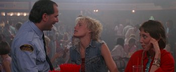 Movie still from “Roxanne” (1987), directed by Fred Schepisi – A man and a woman talking in front of a group of people; Medium shot, Over the shoulder angle