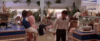 Movie still from “Roxanne” (1987), directed by Fred Schepisi – A group of people sitting at tables in a room; Wide shot, Over the shoulder angle