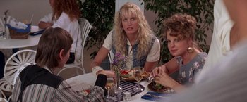 Movie still from “Roxanne” (1987), directed by Fred Schepisi – A group of people sitting at a table with plates of food on it; Medium shot, Over the shoulder angle