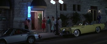 Movie still from “Roxanne” (1987), directed by Fred Schepisi – A group of people standing on a sidewalk near a building; Wide shot, Low angle