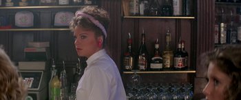 Movie still from “Roxanne” (1987), directed by Fred Schepisi – A woman standing in front of a bar filled with bottles; Close Up shot, Over the shoulder angle