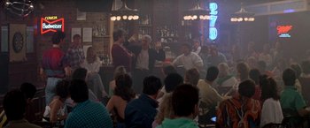 Movie still from “Roxanne” (1987), directed by Fred Schepisi – A group of people sitting in front of a bar; Wide shot, Over the shoulder angle