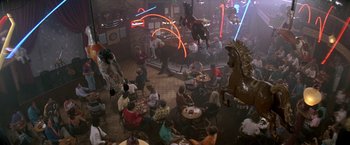 Movie still from “Roxanne” (1987), directed by Fred Schepisi – A group of people sitting at tables in a room; Extreme Wide shot, High angle