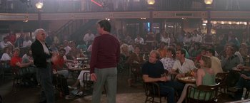 Movie still from “Roxanne” (1987), directed by Fred Schepisi – A group of people sitting and standing in a room; Wide shot, Over the shoulder angle