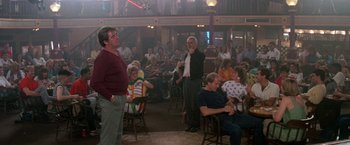 Movie still from “Roxanne” (1987), directed by Fred Schepisi – A group of people sitting in chairs in a room; Wide shot, Over the shoulder angle