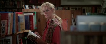 Movie still from “Roxanne” (1987), directed by Fred Schepisi – A woman in a red shirt is reading a book in a library; Medium shot, Over the shoulder angle