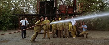 Movie still from “Roxanne” (1987), directed by Fred Schepisi – A group of men in yellow jackets are spraying water from a fire hose; Wide shot, Over the shoulder angle