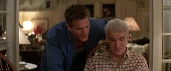 Movie still from “Roxanne” (1987), directed by Fred Schepisi – A man standing next to another man in a room; Medium shot, Over the shoulder angle