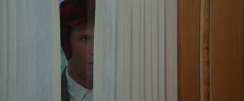 Movie still from “Roxanne” (1987), directed by Fred Schepisi – A man looking out of a window with a red hat on; Close Up shot, Over the shoulder angle