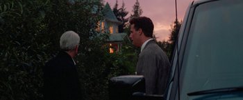 Movie still from “Roxanne” (1987), directed by Fred Schepisi – A man in a suit and tie standing next to another man in front of a house; Medium shot, Low angle