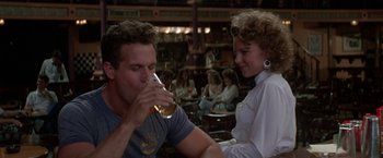 Movie still from “Roxanne” (1987), directed by Fred Schepisi – A man and a woman sitting at a table drinking beer; Medium shot, Over the shoulder angle
