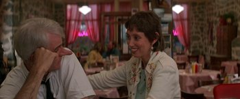 Movie still from “Roxanne” (1987), directed by Fred Schepisi – A woman sitting at a table in a restaurant smiling; Close Up shot, Over the shoulder angle