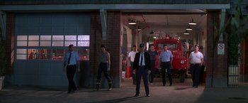Movie still from “Roxanne” (1987), directed by Fred Schepisi – A group of men standing in front of a fire truck; Wide shot, Low angle