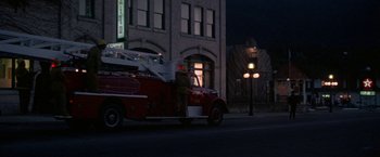 Movie still from “Roxanne” (1987), directed by Fred Schepisi – A man standing next to an old fire truck on the side of the road; Extreme Wide shot, High angle