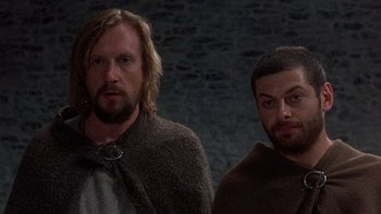 Movie still from “Royal Deceit” (1994), directed by Gabriel Axel – Two men standing next to each other in front of a brick wall; Medium shot, Low angle