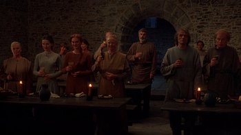 Movie still from “Royal Deceit” (1994), directed by Gabriel Axel – A group of people standing around a table with a candle; Wide shot, High angle