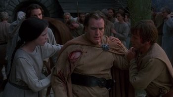 Movie still from “Royal Deceit” (1994), directed by Gabriel Axel – A man with a wound on his arm is being held by a woman; Medium shot, Over the shoulder angle
