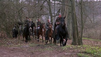 Movie still from “Royal Deceit” (1994), directed by Gabriel Axel – A group of people riding horses through the woods; Wide shot, Low angle