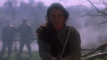 Movie still from “Royal Deceit” (1994), directed by Gabriel Axel – A young man holding a sword in a field; Medium shot, Low angle