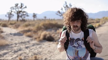 A man with curly hair holding a backpack in the desert