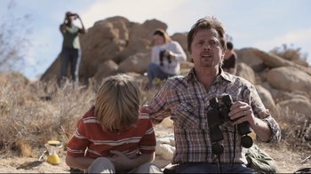 A man holding a camera while sitting next to another man