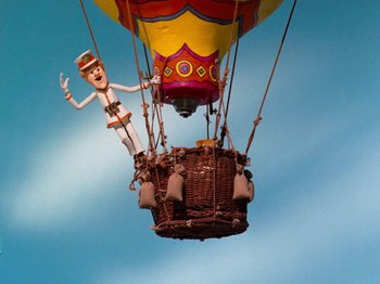 Movie still from “Rudolph and Frosty's Christmas in July” (1979), directed by Jules Bass – A balloon with a character on top of it flying through the air; Wide shot, Low angle