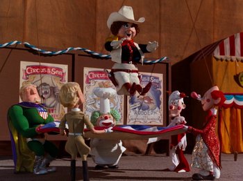 Movie still from “Rudolph and Frosty's Christmas in July” (1979), directed by Jules Bass – A group of people standing in front of a table; Wide shot, Low angle
