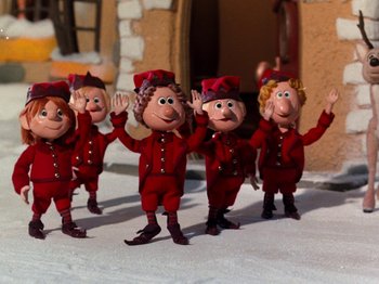 Movie still from “Rudolph and Frosty's Christmas in July” (1979), directed by Jules Bass – A group of people dressed in red standing next to each other; Medium shot, Low angle