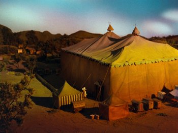 Movie still from “Rudolph and Frosty's Christmas in July” (1979), directed by Jules Bass – A tent in the middle of the desert with mountains in the background; Extreme Wide shot, High angle