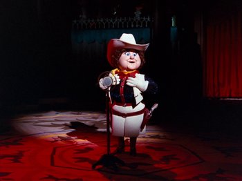 Movie still from “Rudolph and Frosty's Christmas in July” (1979), directed by Jules Bass – A statue of a man dressed as a cowboy holding a cane; Wide shot, Low angle