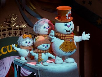 Movie still from “Rudolph and Frosty's Christmas in July” (1979), directed by Jules Bass – A group of snowmen sitting next to each other on top of a table; Medium shot, Low angle