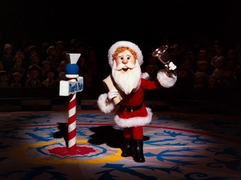 Movie still from “Rudolph and Frosty's Christmas in July” (1979), directed by Jules Bass – A santa clause figure is standing in front of a microphone; Wide shot, Low angle