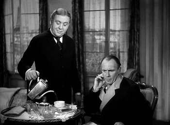 Movie still from “Ruggles of Red Gap” (1935), directed by Leo McCarey – A man sitting at a table talking on the phone while another man pours a cup; Medium shot, High angle