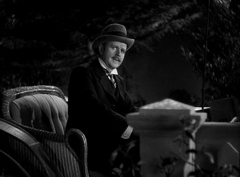 Movie still from “Ruggles of Red Gap” (1935), directed by Leo McCarey – A man in a suit and hat sitting on a chair; Medium shot, Low angle