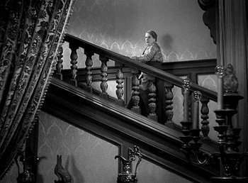 Movie still from “Ruggles of Red Gap” (1935), directed by Leo McCarey – An older woman sitting on a wooden stair case railing; Wide shot, High angle
