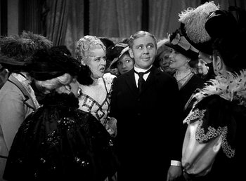 Movie still from “Ruggles of Red Gap” (1935), directed by Leo McCarey – A man and a woman standing next to each other in front of a crowd; Medium shot, Over the shoulder angle