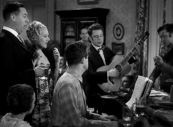 Movie still from “Ruggles of Red Gap” (1935), directed by Leo McCarey – A group of people standing around a table with musical instruments; Medium shot, High angle