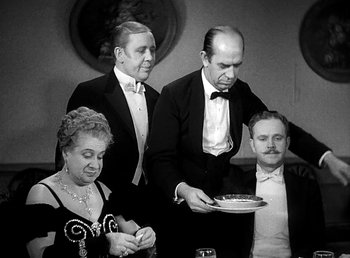 Movie still from “Ruggles of Red Gap” (1935), directed by Leo McCarey – A group of people in formal wear standing around a table; Medium shot, High angle