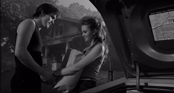 Movie still from “Rumble Fish” (1983), directed by Francis Ford Coppola – A man and a woman standing next to each other in front of an open trunk of a car; Medium shot, Over the shoulder angle