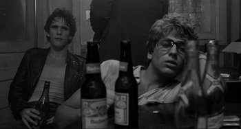 Movie still from “Rumble Fish” (1983), directed by Francis Ford Coppola – Two young men sitting at a table with beer bottles; Medium shot, Over the shoulder angle