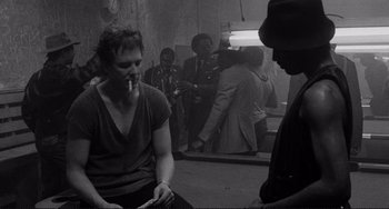 Movie still from “Rumble Fish” (1983), directed by Francis Ford Coppola – A group of people in a room smoking; Medium shot, Over the shoulder angle