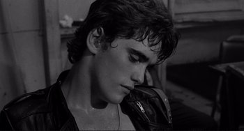Movie still from “Rumble Fish” (1983), directed by Francis Ford Coppola – A young man with wet hair is holding a leather bag; Close Up shot, High angle